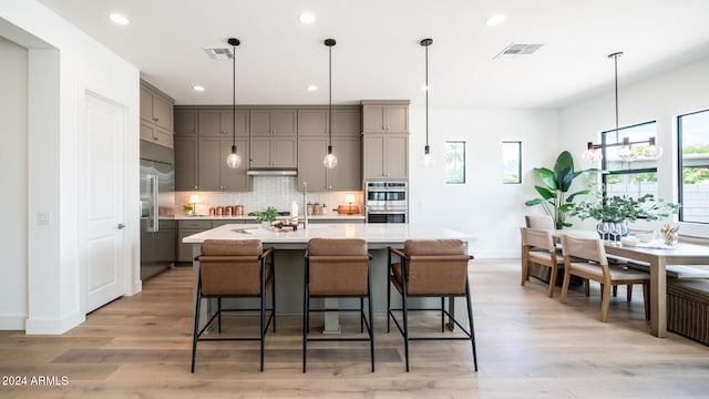 kitchen with appliances with stainless steel finishes, gray cabinetry, light hardwood / wood-style floors, a breakfast bar area, and an island with sink