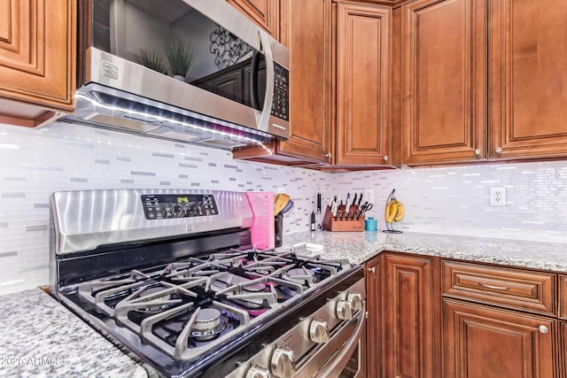 3823 E Kroll Dr, Gilbert, AZ 85234 - kitchen with stainless steel appliances, tasteful backsplash, brown cabinets, and light stone counters