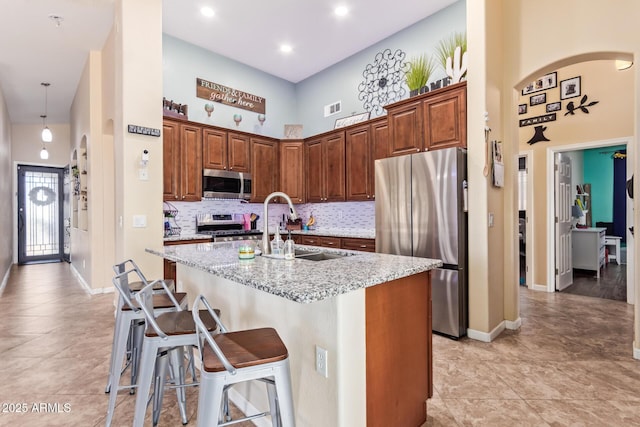 3823 E Kroll Dr, Gilbert, AZ 85234 - kitchen featuring appliances with stainless steel finishes, an island with sink, light stone counters, a high ceiling, and backsplash