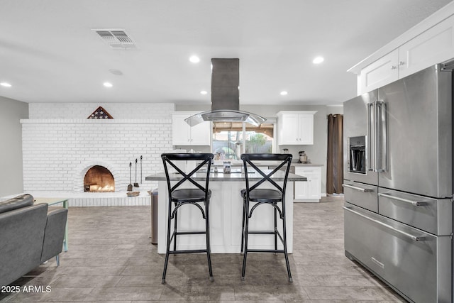 kitchen with white cabinets, a center island, a kitchen bar, island range hood, and high end fridge