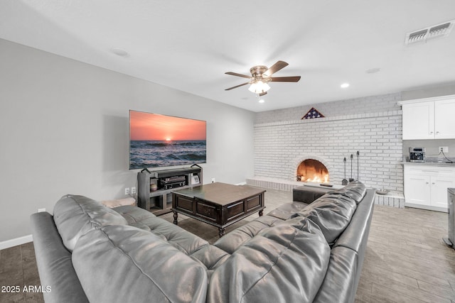 living room with a brick fireplace, light hardwood / wood-style floors, and ceiling fan