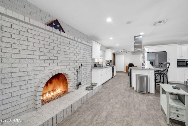 kitchen featuring high quality fridge, a fireplace, white cabinetry, island range hood, and a kitchen island