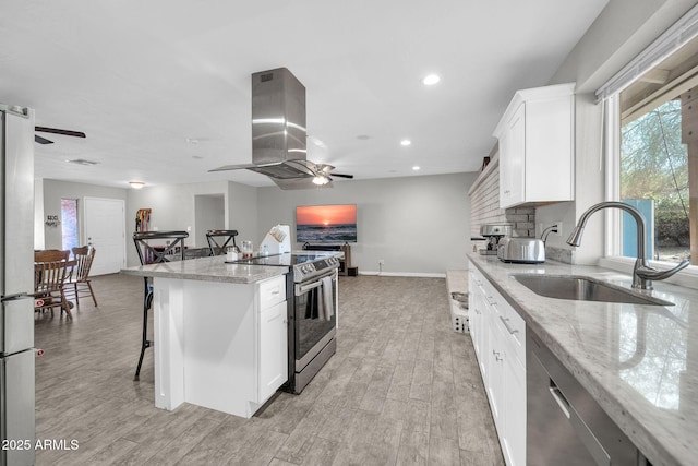 kitchen featuring appliances with stainless steel finishes, sink, white cabinetry, light stone countertops, and island range hood