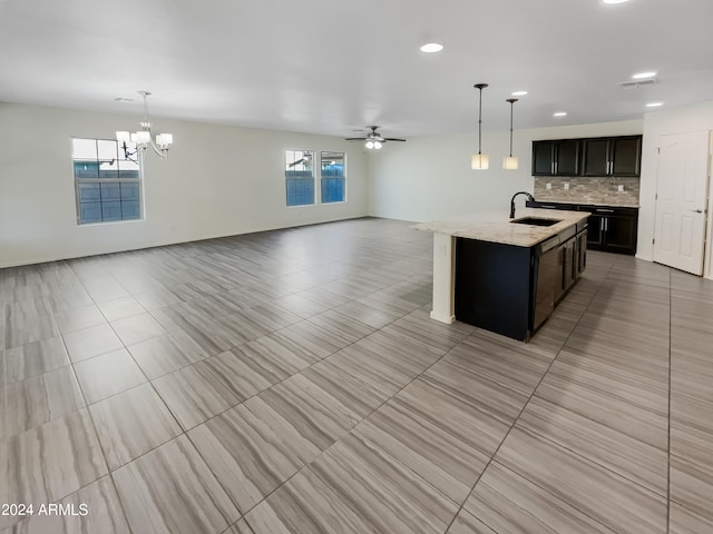 kitchen with a center island with sink, backsplash, light tile floors, hanging light fixtures, and sink