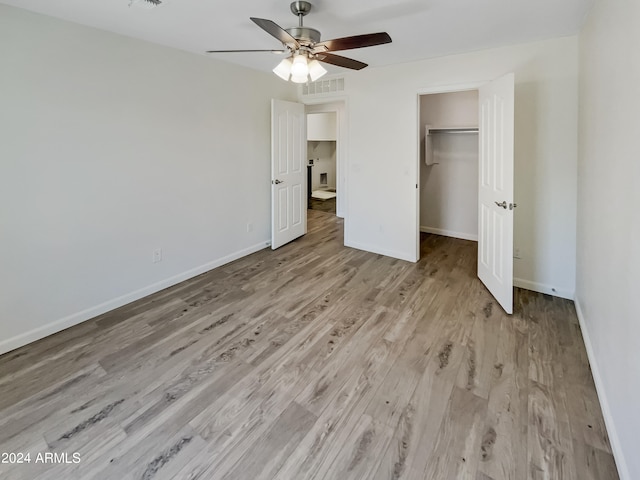 unfurnished bedroom with a walk in closet, a closet, ceiling fan, and light wood-type flooring