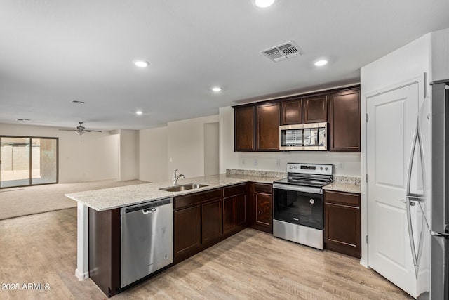 kitchen with sink, light stone counters, kitchen peninsula, stainless steel appliances, and light hardwood / wood-style floors