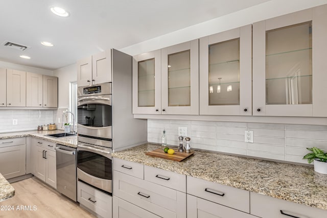 kitchen featuring backsplash, light stone countertops, sink, and light hardwood / wood-style flooring