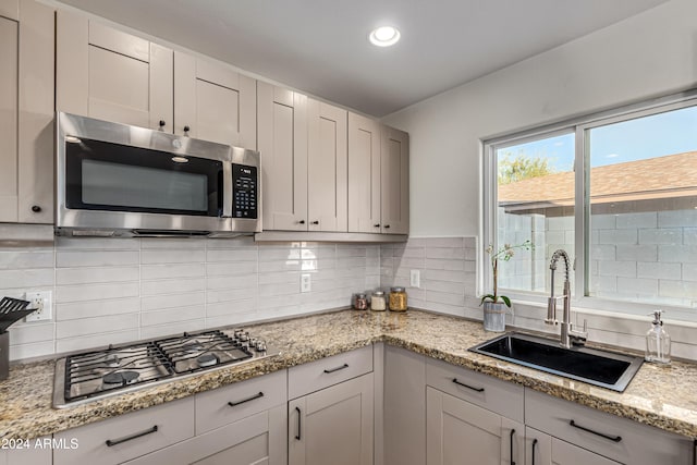 kitchen with light stone countertops, backsplash, stainless steel appliances, sink, and white cabinetry