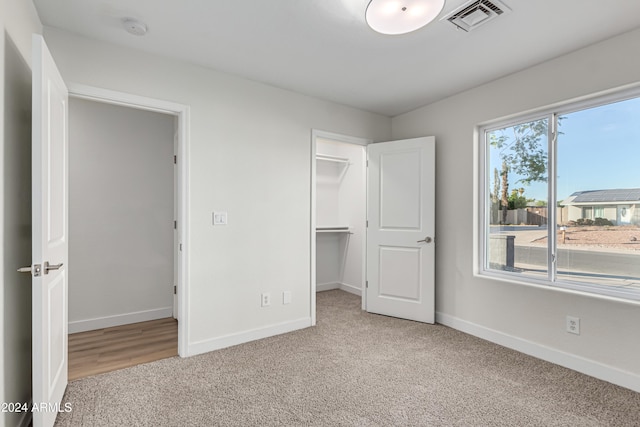 unfurnished bedroom with a walk in closet, light carpet, and a closet