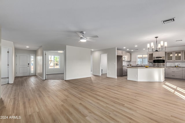 unfurnished living room featuring ceiling fan with notable chandelier, light wood-type flooring, and sink