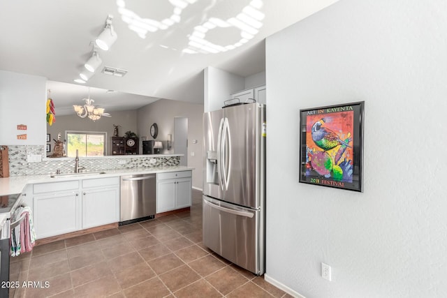 kitchen with appliances with stainless steel finishes, sink, white cabinets, a chandelier, and decorative backsplash