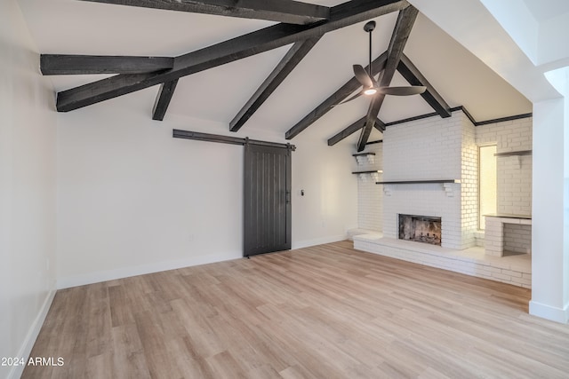 unfurnished living room with light hardwood / wood-style floors, a barn door, a brick fireplace, vaulted ceiling with beams, and ceiling fan