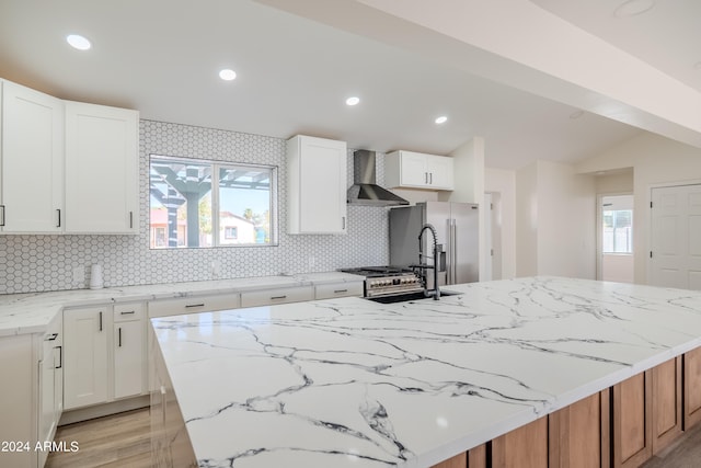 kitchen featuring white cabinetry, a center island, wall chimney range hood, and tasteful backsplash