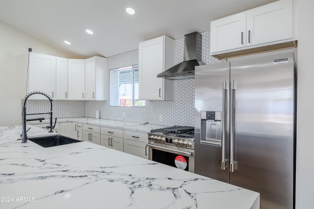 kitchen with white cabinetry, wall chimney range hood, premium appliances, backsplash, and light stone countertops