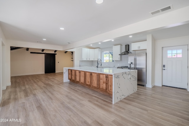 kitchen featuring white cabinets, a barn door, a large island, wall chimney range hood, and high end fridge