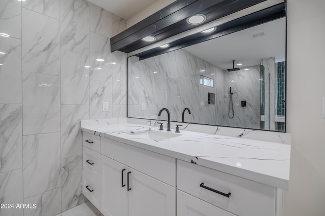 bathroom with a tile shower, vanity, and tile walls