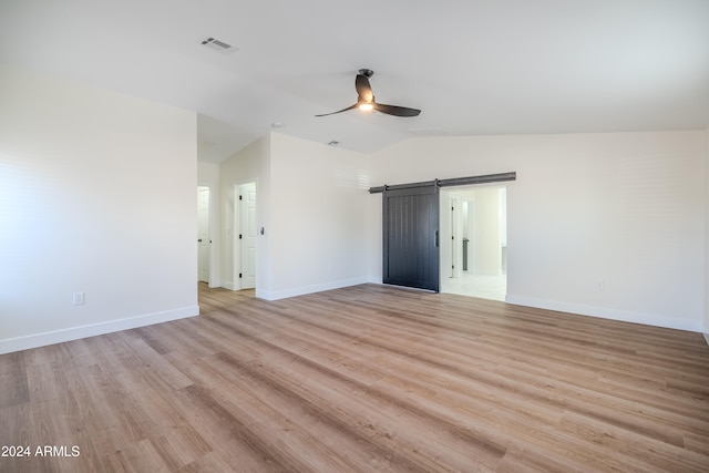 unfurnished room featuring ceiling fan, light wood-type flooring, a barn door, and lofted ceiling