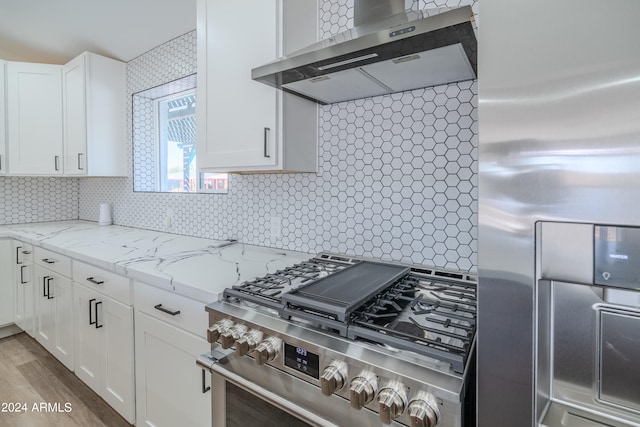 kitchen with light wood-type flooring, tasteful backsplash, white cabinetry, wall chimney range hood, and high quality appliances