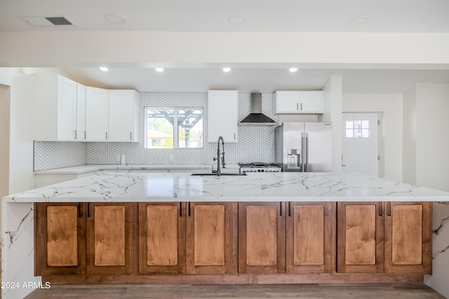 kitchen with light stone counters, white cabinets, wall chimney range hood, light hardwood / wood-style flooring, and stainless steel appliances