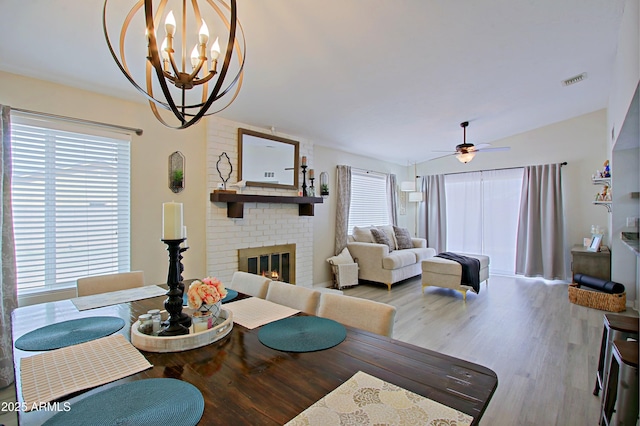 living area featuring ceiling fan with notable chandelier, wood finished floors, a brick fireplace, and a healthy amount of sunlight