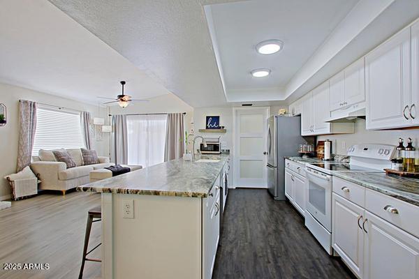 kitchen featuring under cabinet range hood, a kitchen breakfast bar, white cabinets, and white range with electric cooktop