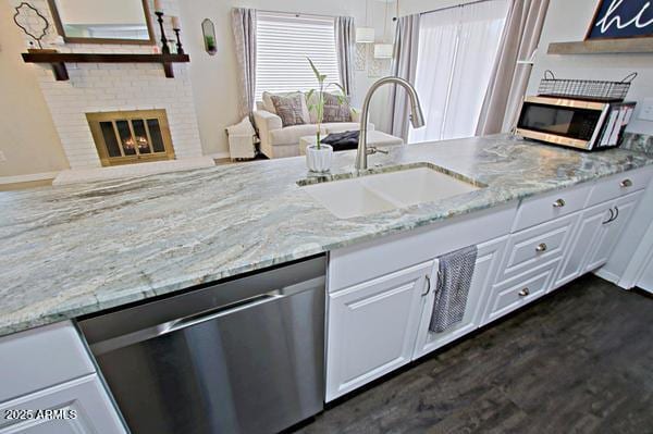 kitchen with light stone countertops, appliances with stainless steel finishes, a glass covered fireplace, white cabinetry, and a sink