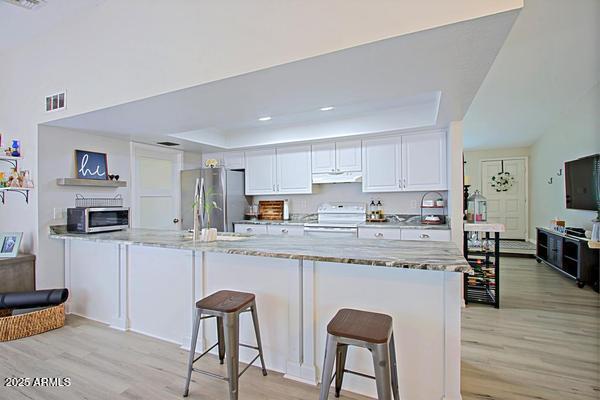 kitchen featuring visible vents, under cabinet range hood, electric range oven, freestanding refrigerator, and white cabinets