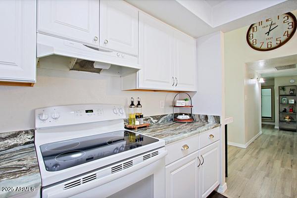 kitchen featuring white electric range, under cabinet range hood, white cabinets, and light wood finished floors