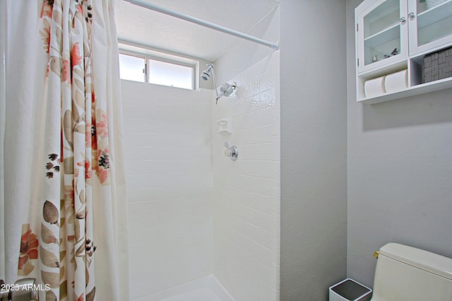 bathroom with a tile shower, toilet, and a textured wall