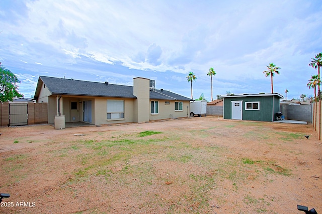 rear view of property featuring an outbuilding, a storage unit, a fenced backyard, and roof with shingles