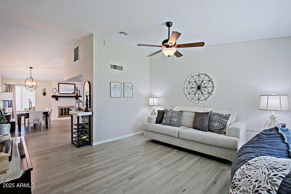 living area with visible vents, baseboards, wood finished floors, and ceiling fan with notable chandelier