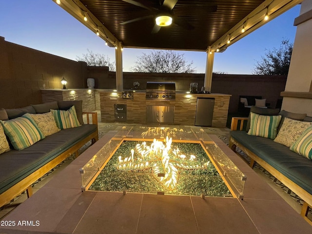 patio terrace at dusk with ceiling fan, exterior kitchen, an outdoor living space, and grilling area