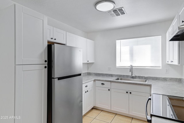 kitchen featuring electric range oven, freestanding refrigerator, white cabinetry, a sink, and light tile patterned flooring