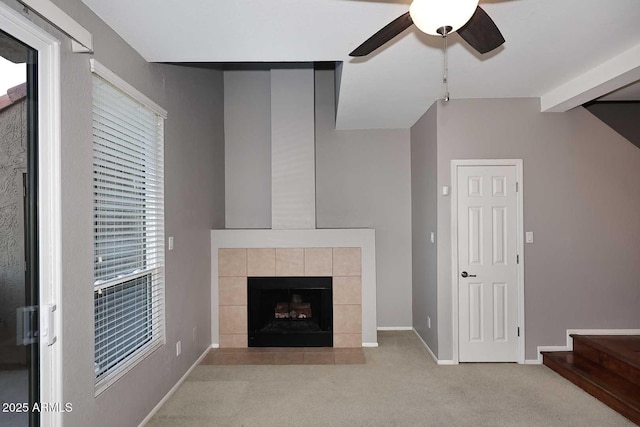 unfurnished living room with a tiled fireplace, vaulted ceiling with beams, light carpet, and ceiling fan