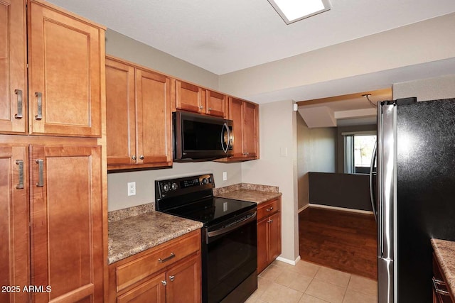 kitchen with light stone counters, black range with electric stovetop, light tile patterned floors, and stainless steel fridge