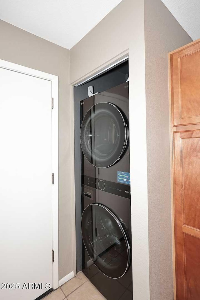 laundry area with stacked washer / dryer and light tile patterned floors