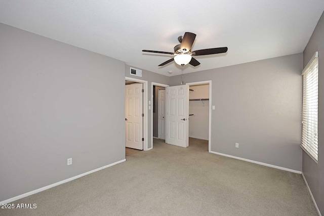 unfurnished bedroom with a walk in closet, light colored carpet, ceiling fan, and a closet