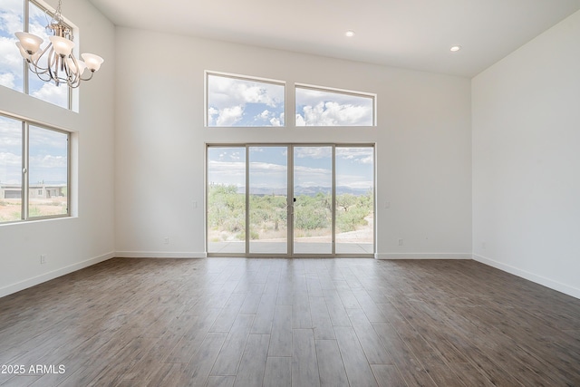 empty room featuring a chandelier, plenty of natural light, a towering ceiling, dark wood-style floors, and baseboards