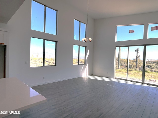 unfurnished living room featuring a towering ceiling, a chandelier, and wood finished floors