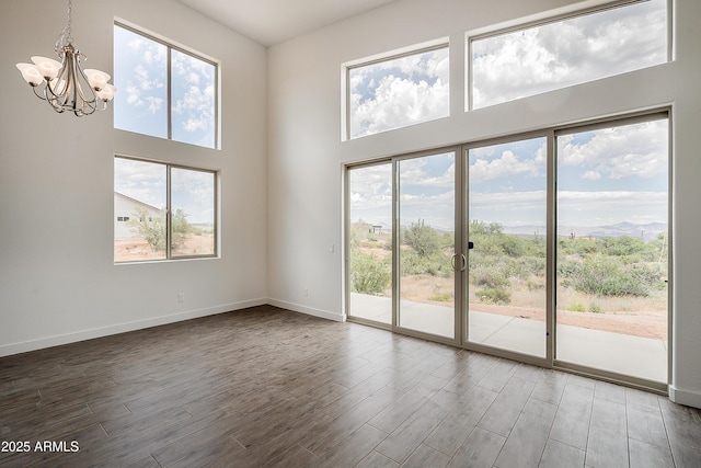 unfurnished living room with a chandelier, wood finished floors, a high ceiling, and baseboards