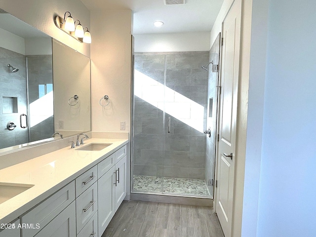 bathroom featuring wood finished floors, a shower stall, double vanity, and recessed lighting