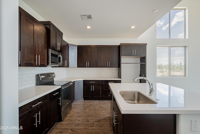 kitchen with stainless steel appliances, a sink, a center island with sink, dark brown cabinets, and recessed lighting