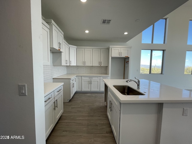 kitchen with a sink, recessed lighting, tasteful backsplash, a kitchen island with sink, and dark wood-type flooring