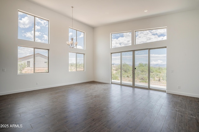 unfurnished living room with a towering ceiling, a chandelier, dark wood-style floors, and baseboards