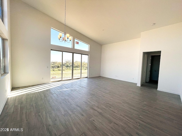 empty room featuring a chandelier, high vaulted ceiling, dark wood-type flooring, and baseboards