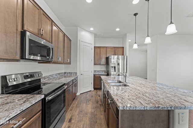 kitchen featuring a kitchen island with sink, a sink, appliances with stainless steel finishes, dark wood finished floors, and decorative light fixtures