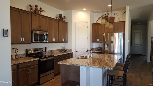 kitchen with appliances with stainless steel finishes, a kitchen breakfast bar, dark wood-style flooring, light stone countertops, and a sink