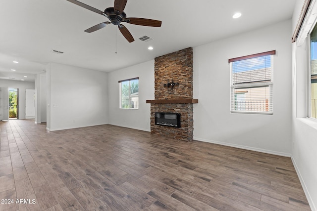 unfurnished living room featuring baseboards, visible vents, wood finished floors, and a stone fireplace