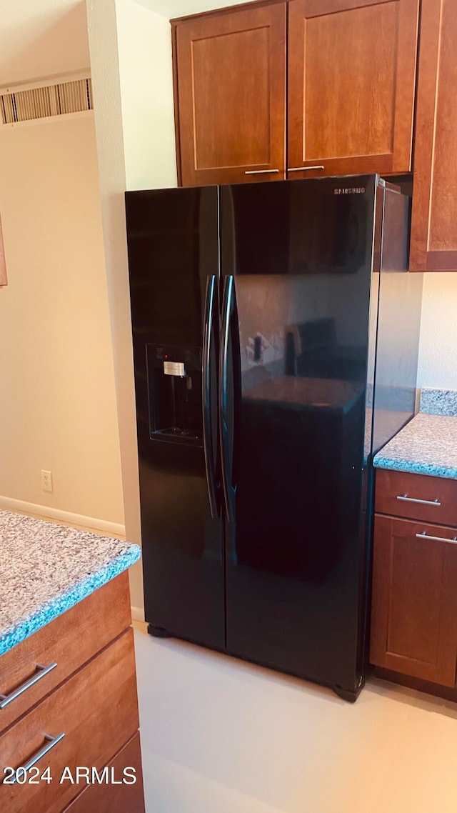 kitchen featuring black fridge with ice dispenser and light stone countertops