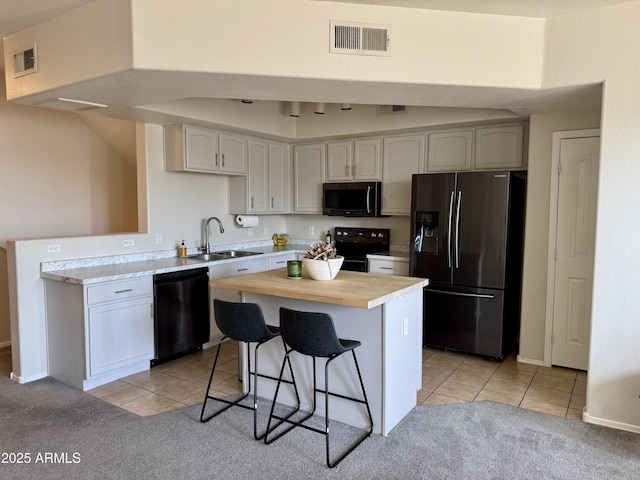 kitchen with sink, a kitchen island, a breakfast bar area, light tile patterned floors, and black appliances